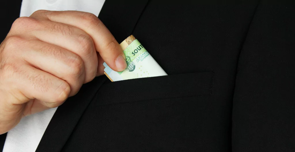 imagem mostra a mão de um homem tirando dinheiro do bolso do terno 