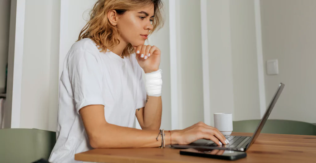 Uma mulher sentada à mesa com seu laptop, com o pulso fraturado