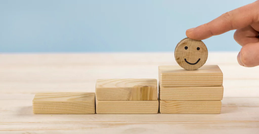 Uma mão empurrando um rosto sorridente em blocos de madeira