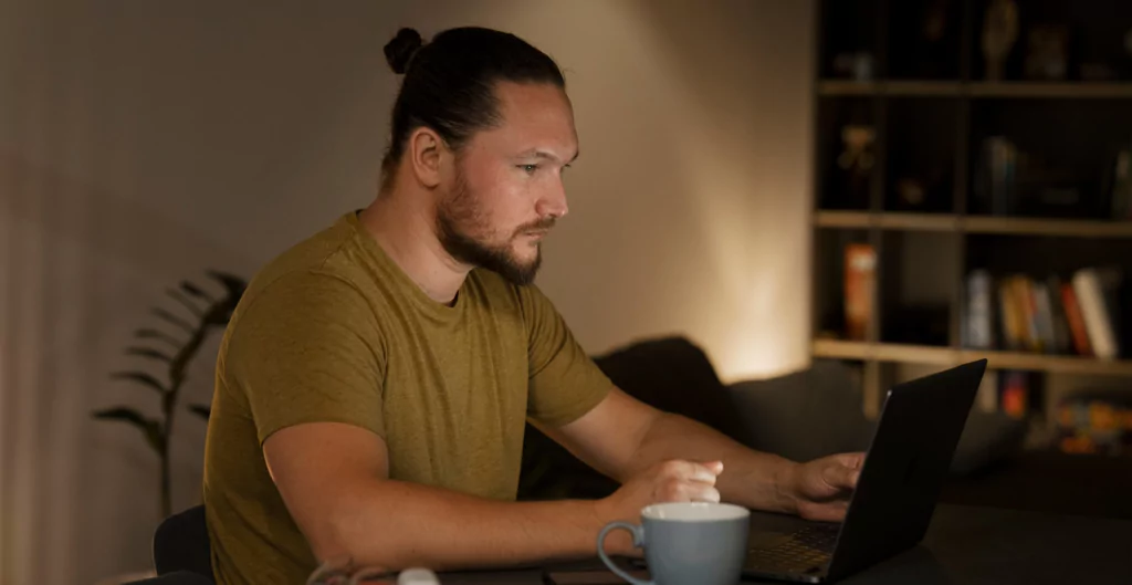 Homem sentado à mesa com um laptop e uma xícara de café