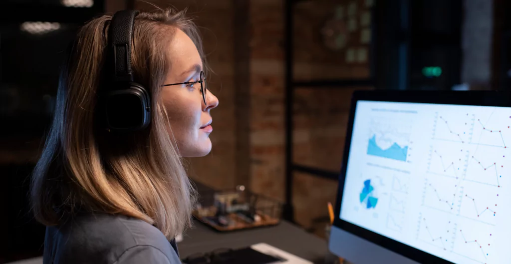 mulher usando fones de ouvido e sentada de frente para o computador 