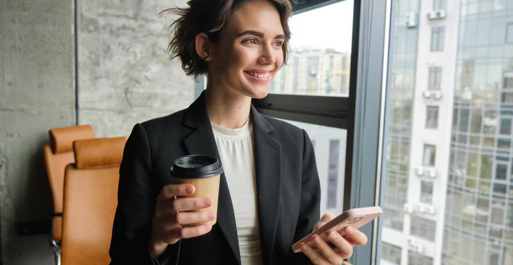 mulher sorridente segurando um copo de café e o celular 