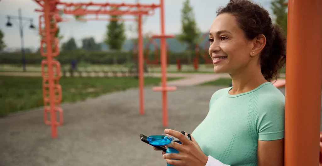 mulher em um parque com uma garrafa de agua e um celular na mão