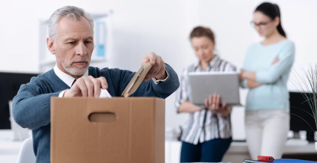 imagem mostra homem com olhar triste guardando objetos em uma caixa de papelão