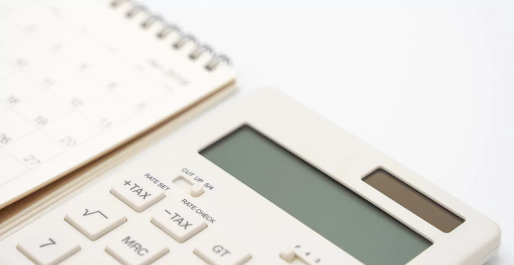 imagem mostra uma calculadora do lado de um bloco de notas com um calendário 