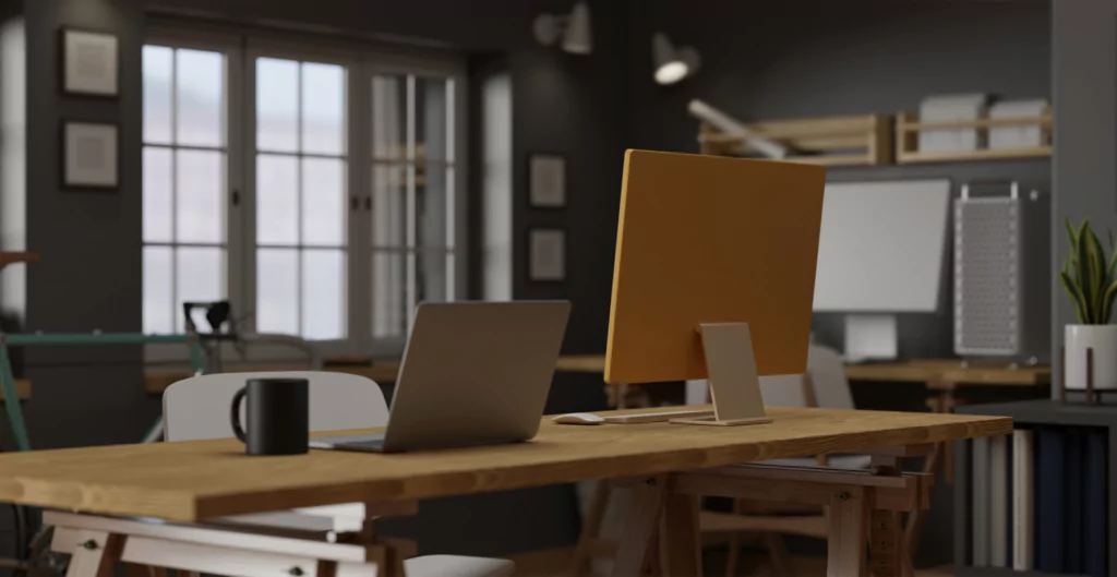 imagem mostra uma mesa com um notebook, um computador e uma caneca de café em um escritório vazio 