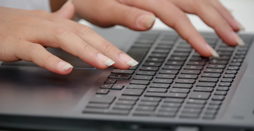 Close-up das mãos de uma mulher digitando em um teclado de laptop, focando na interação com a tecnologia