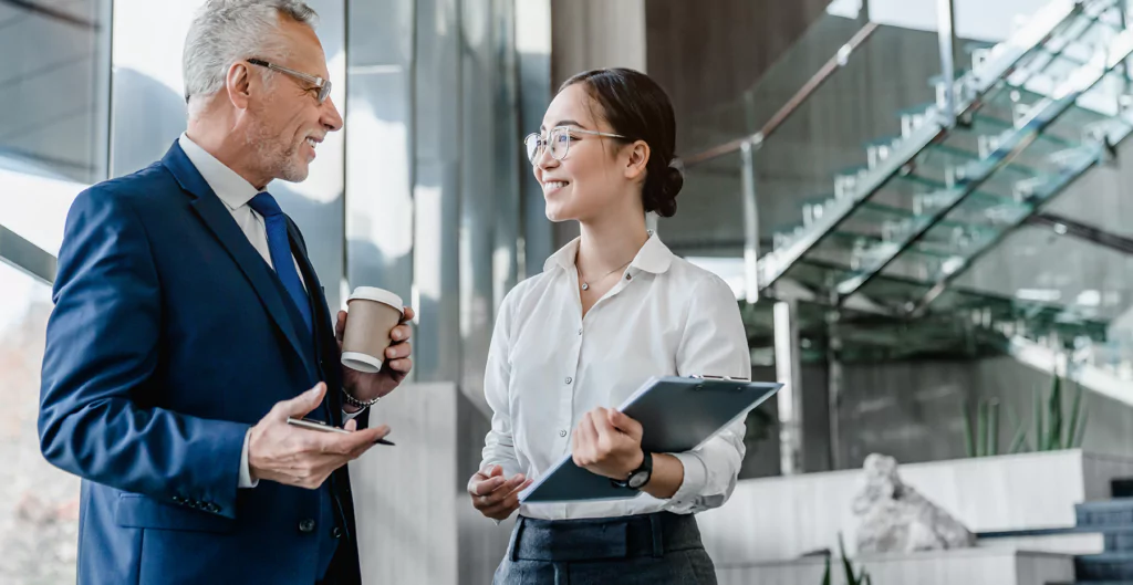 Homem idoso e mulher jovem conversando e segurando copos de café em um ambiente corporativo moderno