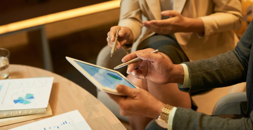 Duas pessoas de negócios analisando gráficos em um tablet durante uma reunião em uma sala de conferência iluminada.
