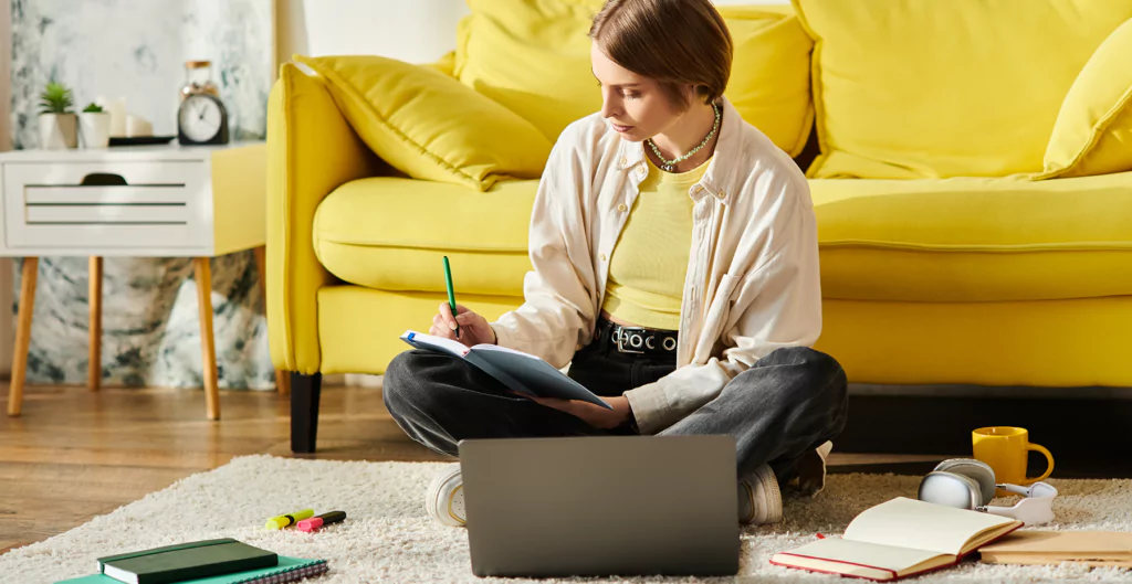 ulher estudando em casa, sentada no tapete com laptop, livros e canecas ao redor