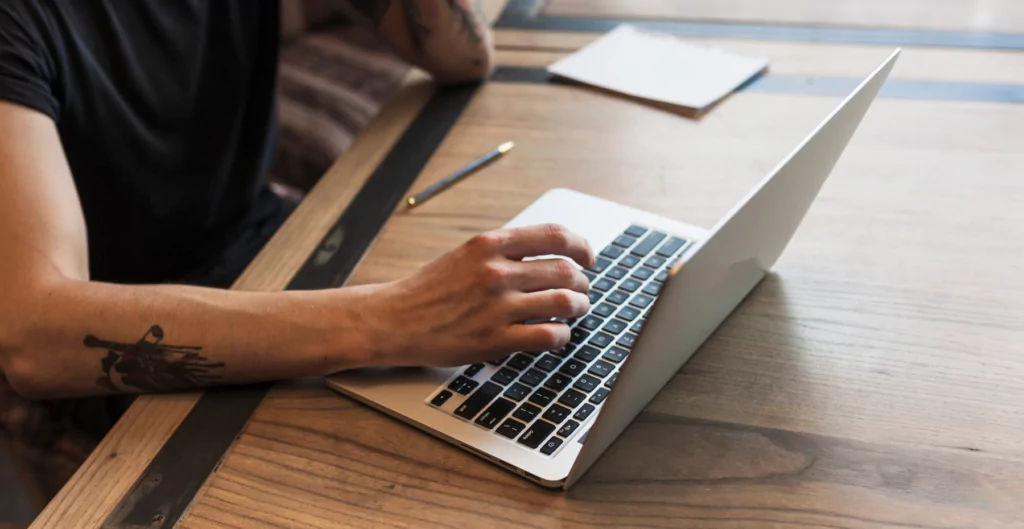 pessoas mexendo um notebook com um bloco para anotações do lado 