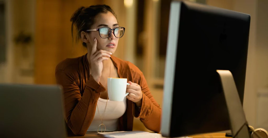 mulher sentada de frente ao computador segurando uma xícara 