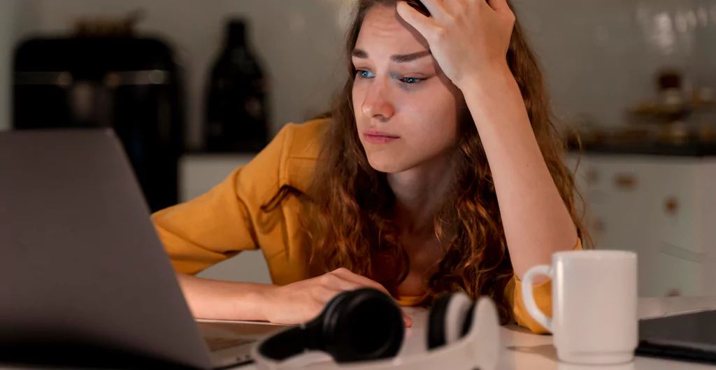 mulher sentada em frente ao notebook com expressão de chateada e com a mão na cabeça 