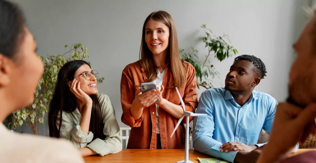 Jovem mulher falando em reunião com colegas ao redor da mesa.