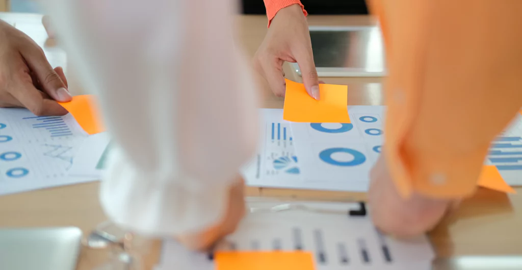 imagem foca em braços colocando post its em papéis com gráficos 