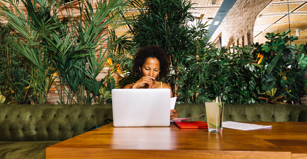 mulher sentada em uma mesa de frente para o notebook em um ambiente com muitas plantas 