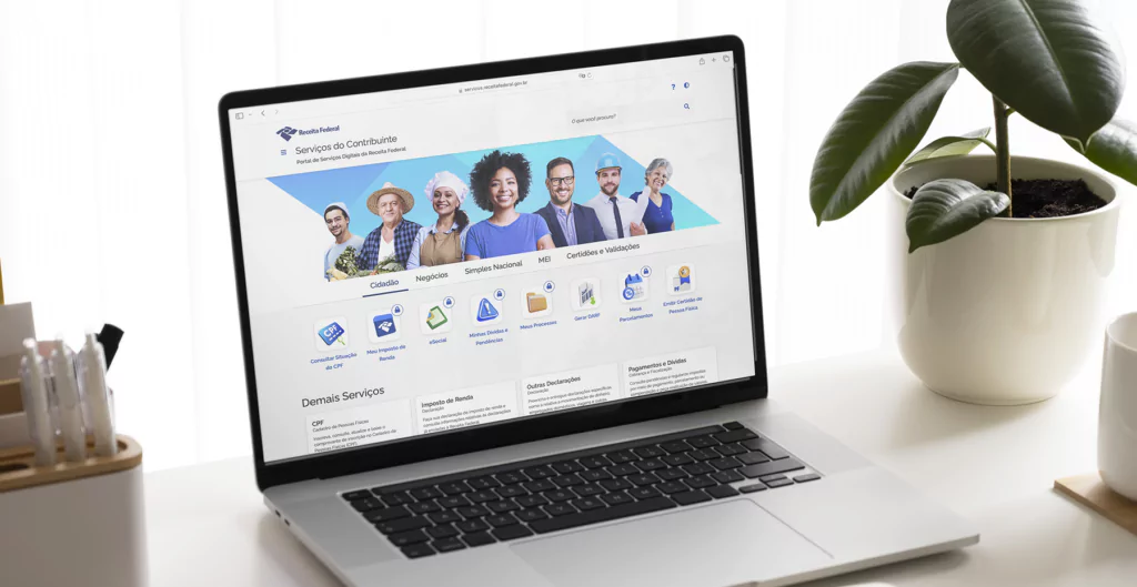 Página inicial do site da Receita Federal exibida em um laptop sobre uma mesa, com planta ao lado.