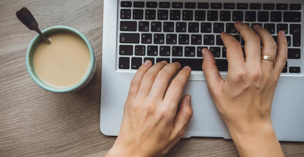 imagem mostra alguém mexendo no notebook e ao lado uma xícara de café com leite 