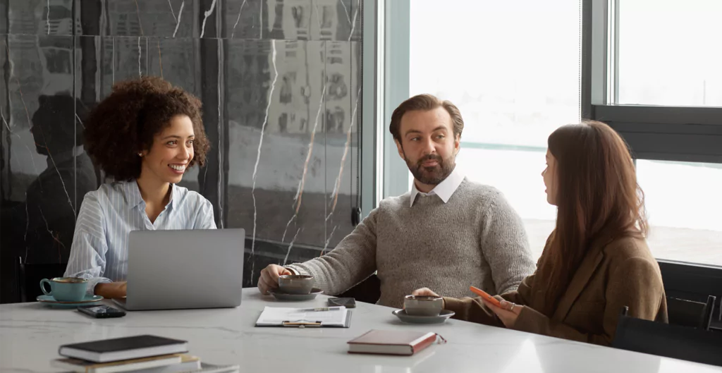  Três colegas de trabalho em reunião casual com laptops e café.