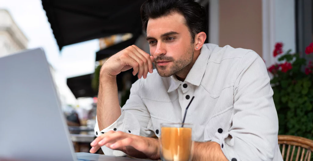 Homem usando laptop em uma cafeteria, com café ao lado.