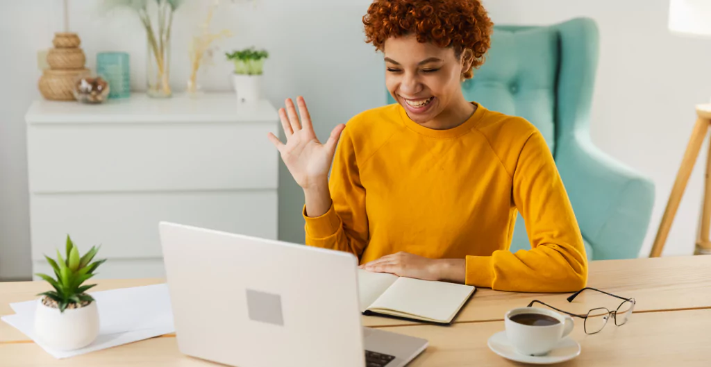 Jovem sorrindo e acenando para a câmera durante chamada online.