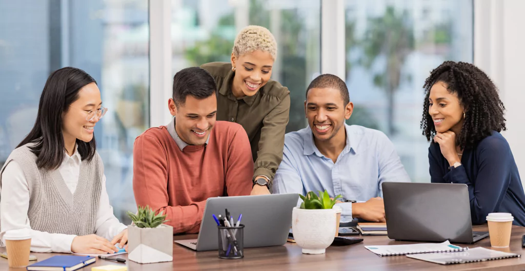 Grupo diverso sorrindo enquanto trabalha em laptops.