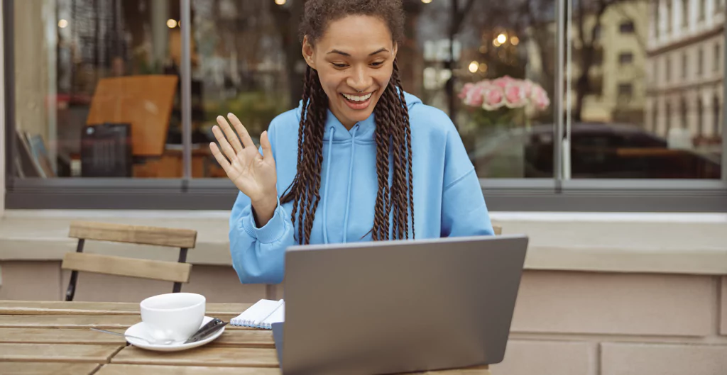 Mulher brasileira acenando durante videoconferência ao ar livre, simbolizando flexibilidade e bem-estar.