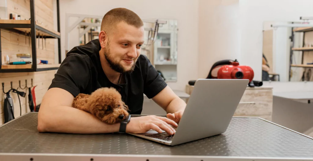 Homem trabalhando com laptop, acompanhado de um cachorro, representando flexibilidade na CLT Premium.