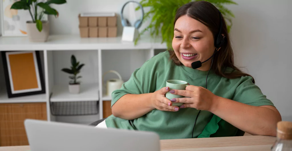 Mulher sorrindo durante videoconferência, com uma xícara nas mãos, ilustrando benefícios do trabalho remoto na CLT Premium.