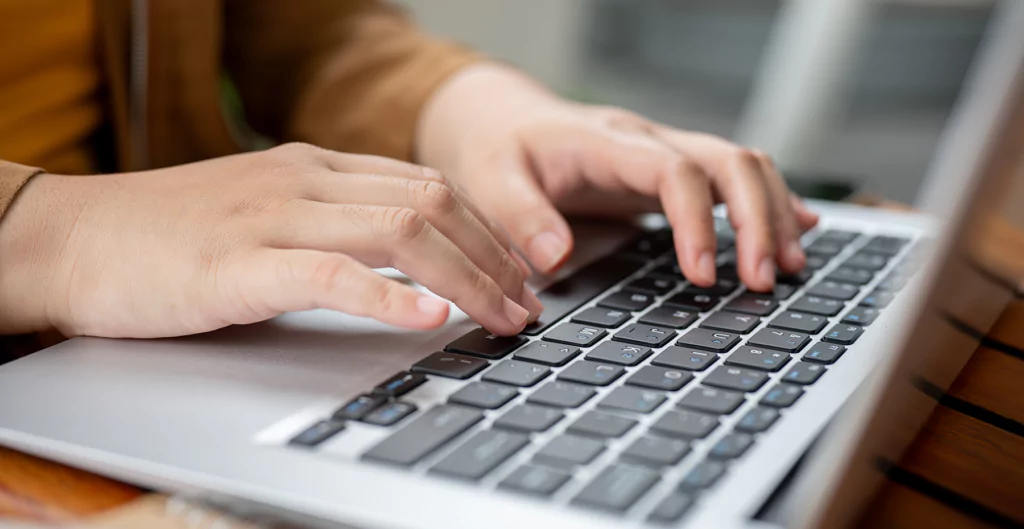 Mãos digitando em um teclado de laptop, sugerindo a redação de um termo de confidencialidade.