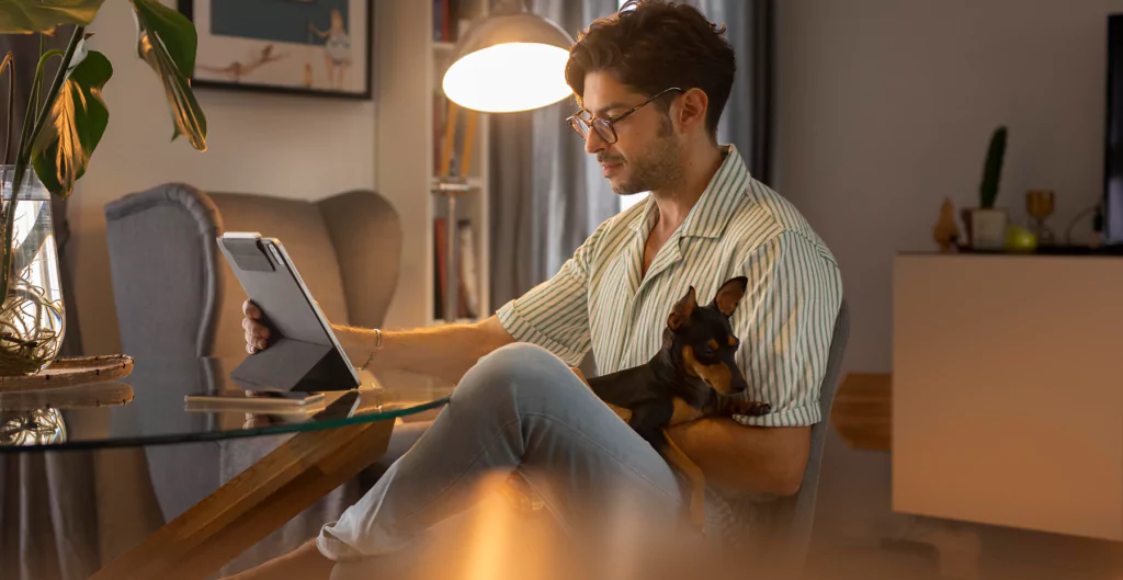 Homem trabalhando com tablet e cachorro no colo, em casa.