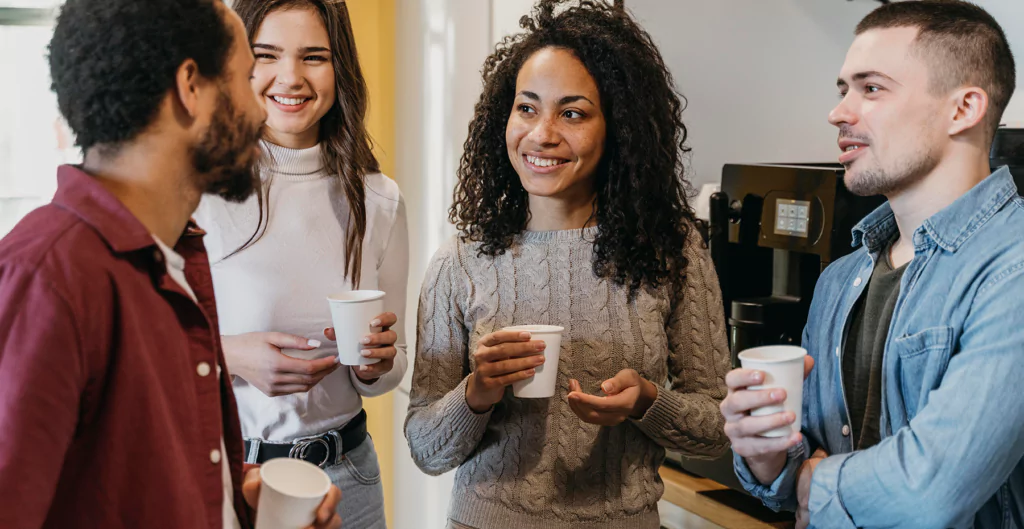 Grupo de colegas de trabalho conversando durante pausa para café.