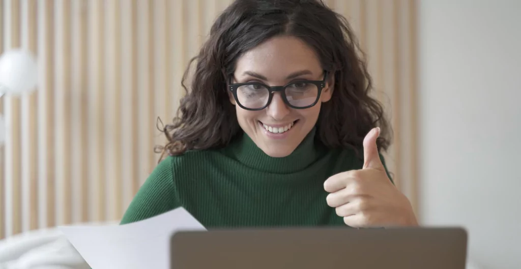 Mulher sorridente dando um joinha durante uma entrevista online.