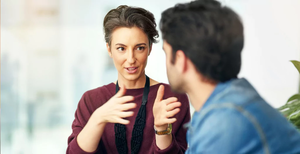 Mulher explicando algo para homem, ilustrando diálogo e cuidado em uma demissão humanizada.