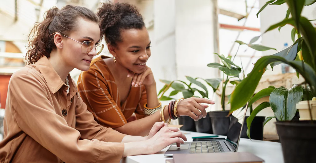 Duas mulheres sentadas à mesa com notebook visualizando a divisão de tarefas