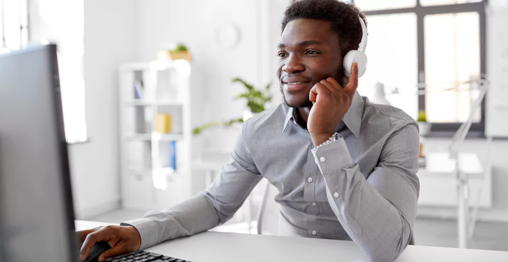 Homem sorridente usando fones de ouvido no escritório, enfatizando o impacto positivo da música para foco e bem-estar no ambiente profissional.