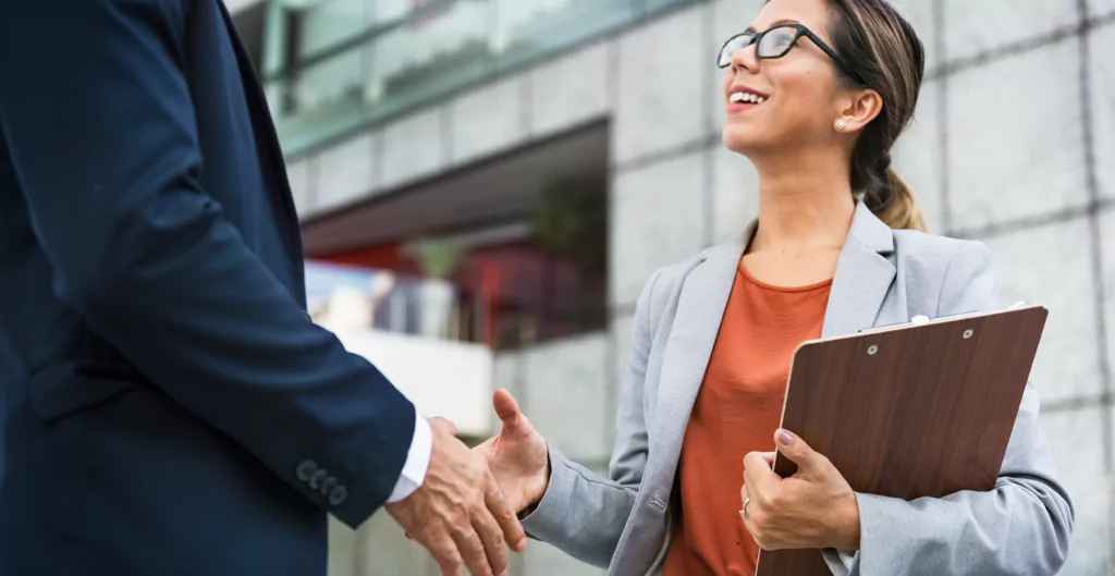 Mulheres de blazer e óculos, apertando a mão de um homem