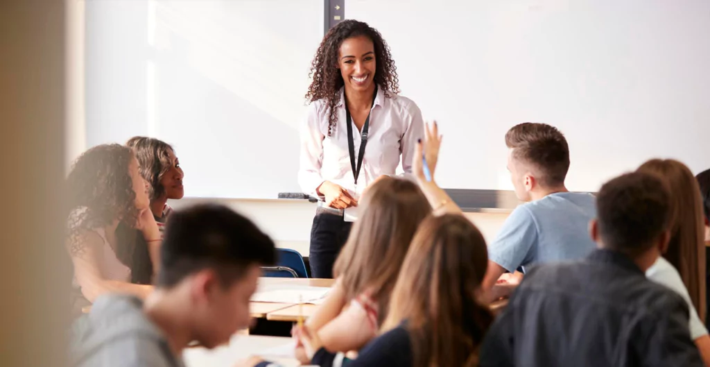 Professora sorridente liderando uma aula, com alunos atentos ao redor, representando treinamento e desenvolvimento profissional.