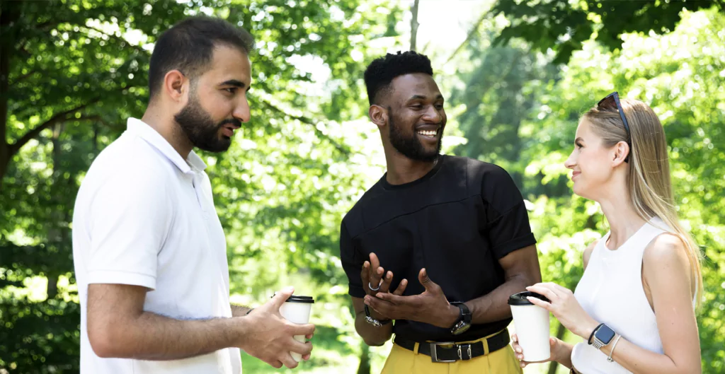 imagem mostra uma mulher e dois homens conversando em um ambiente aberto 