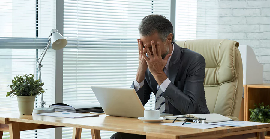 Ambiente corporativo, com um homem com às mãos no rosto, demostrando ansiedade no trabalho 