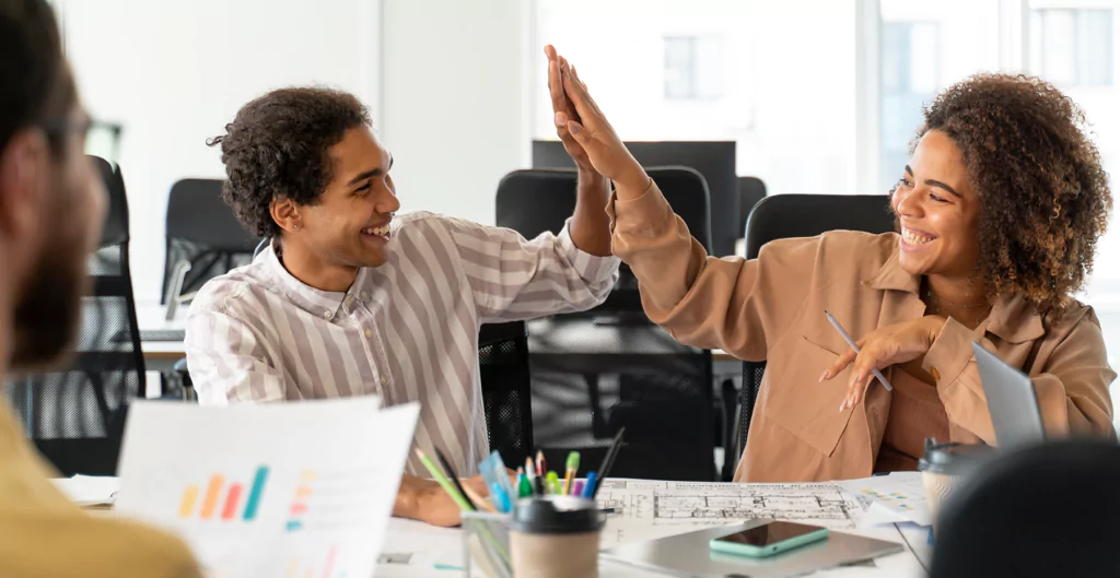 Dois colegas de trabalho comemorando juntos, mostrando o interesse dos colaboradores no sucesso do projeto.