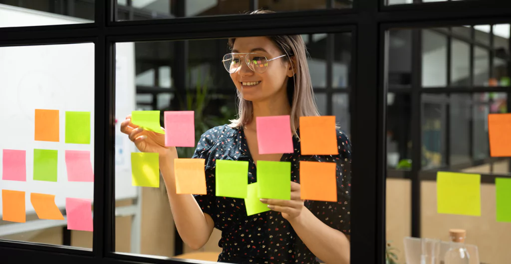 Mulher organizando post-its coloridos para planejar tarefas no escritório.