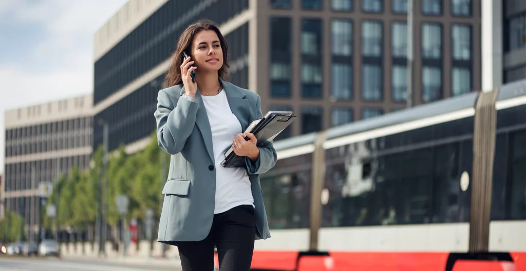 mulher em pé com o celular na orelha, segurando papéis e um notebook. Imagem representa a transição de carreira na maturidade