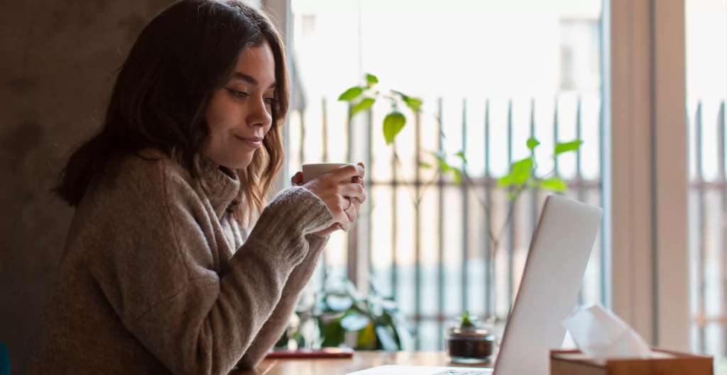 mulher com uma xícara na mão e olhando para o computador 