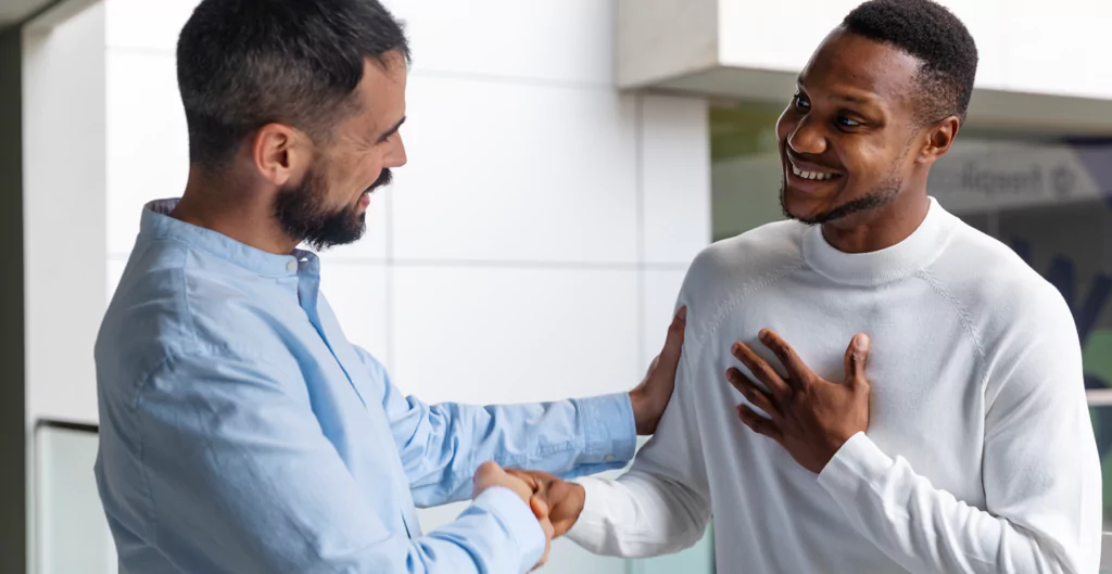 Dois homem sorrindo com roupas socais apertando as mãos.