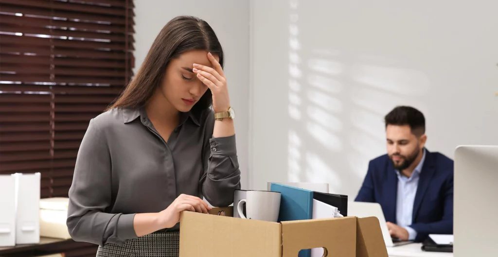 mulher pensativa com uma mão na testa e a outra em uma caixa, representando o revenge quitting