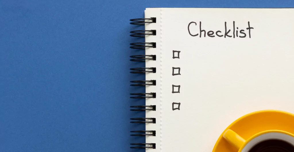 Imagem de um caderno espiral aberto com uma lista de verificação e uma xícara amarela de café ao lado sobre uma mesa azul.