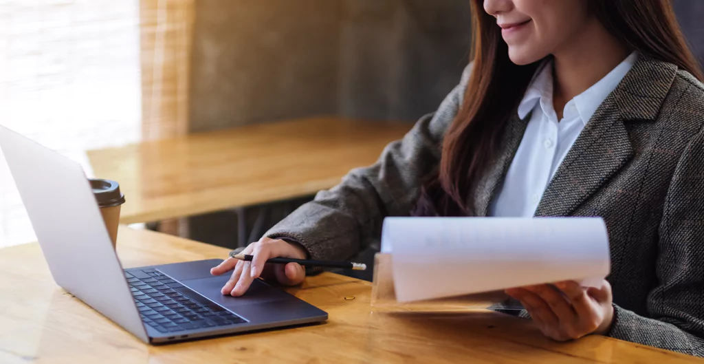 Mulher analisa documentos no notebook em ambiente corporativo, representando análise de vínculos entre doenças ocupacionais e funções via NTEP.