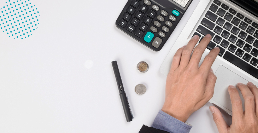 imagem de um homem digitando no computador com uma calculadora, uma caneta e duas moedas ao lado